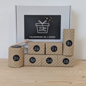 Sept étuis kraft numérotés du Calendrier de l'Après disposés en escalier devant la boîte de la marque, cuillère à miel en bois