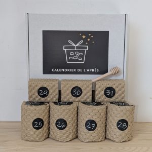 Boîte blanche Calendrier de l'Après et ses sept étuis kraft numérotés photographiés sur fond clair et table en bois
