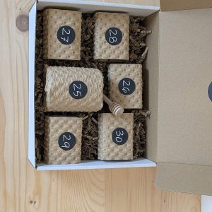 Coffret Calendrier de l'Après ouvert vu de dessus sur une table en bois clair, étuis kraft carrés et cuillère à miel
