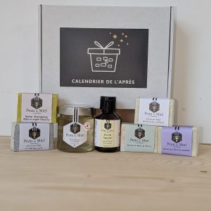 Ensemble des produits du Calendrier de l'Après, savons Peau de Miel dans leurs étuis, pot de miel et flacon ambré devant la boîte blanche