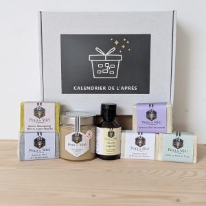 Les produits du Calendrier de l'Après alignés devant la boîte, savons Peau de Miel dans leurs étuis, pot de miel et flacon ambré