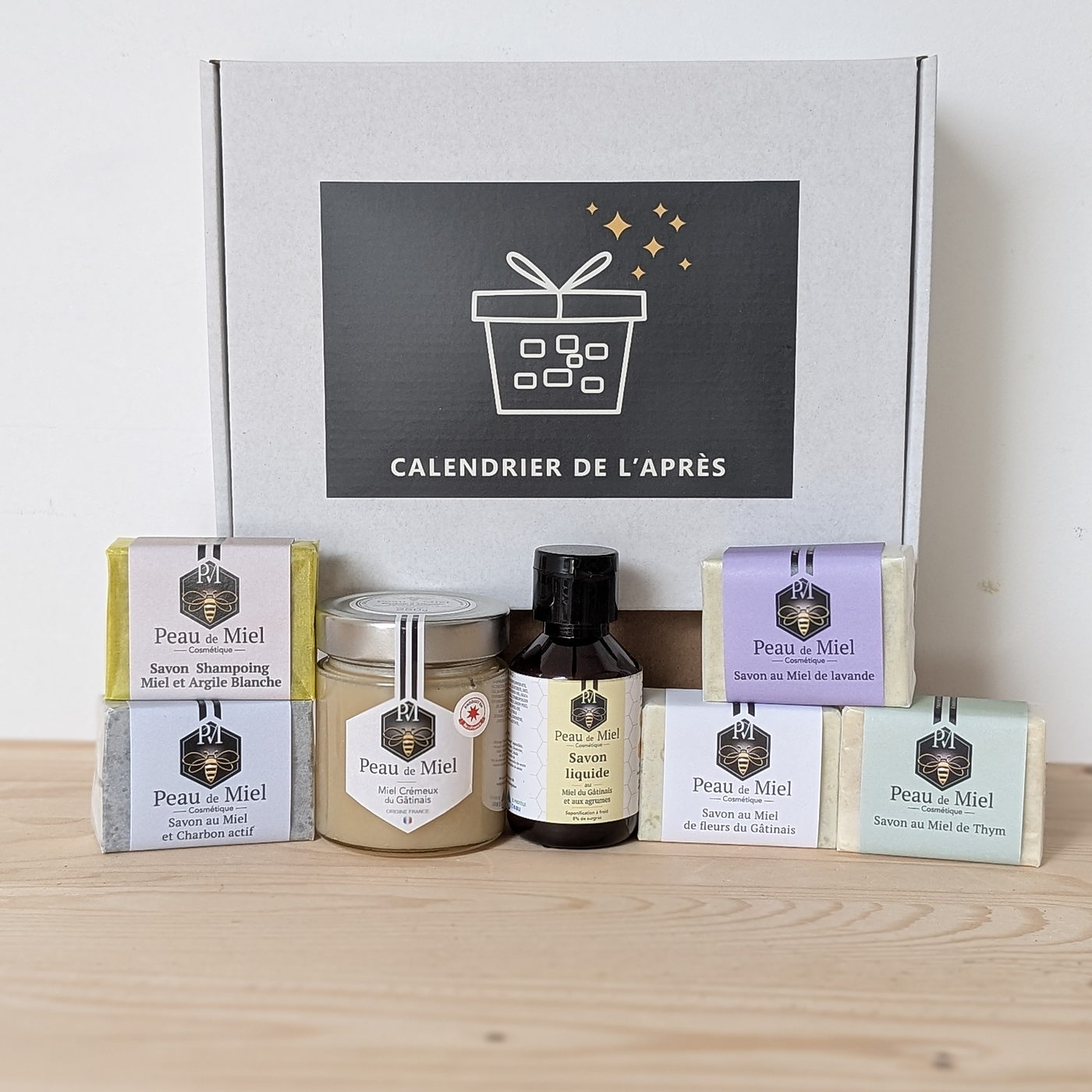 Les produits du Calendrier de l'Après alignés devant la boîte, savons Peau de Miel dans leurs étuis, pot de miel et flacon ambré