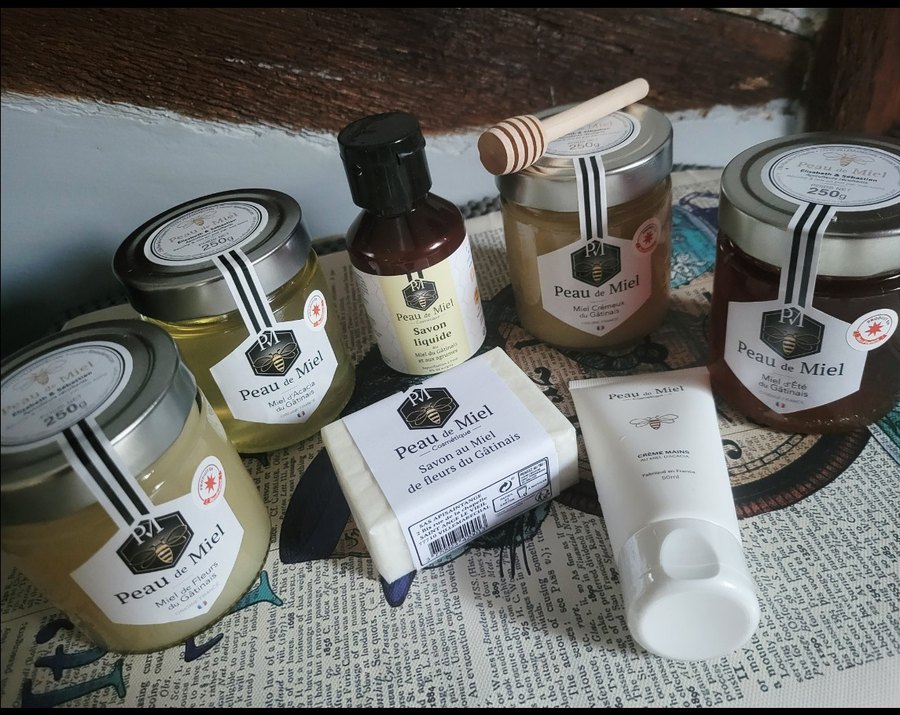 Quatre pots de miel du Gâtinais, un savon, un savon liquide, une crème pour les mains et une cuillère en bois, sortis de leurs étuis